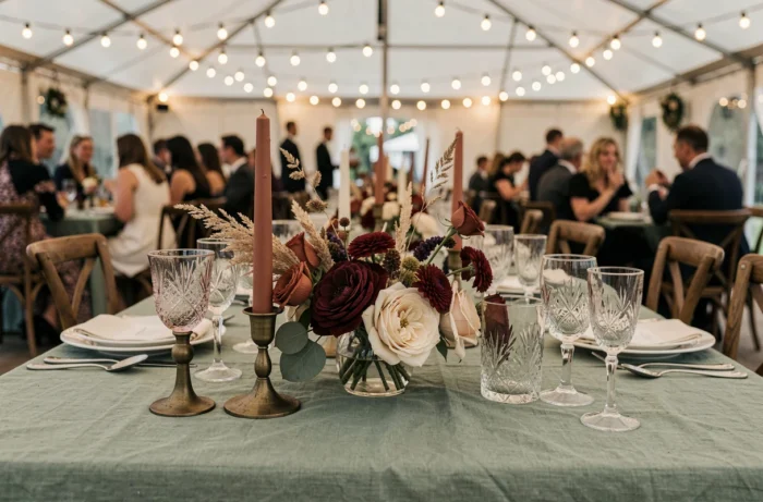 Décoration de table de mariage élégante avec fleurs séchées en teintes terracotta et bordeaux, bougies en laiton et verrerie vintage sous une tente de réception
